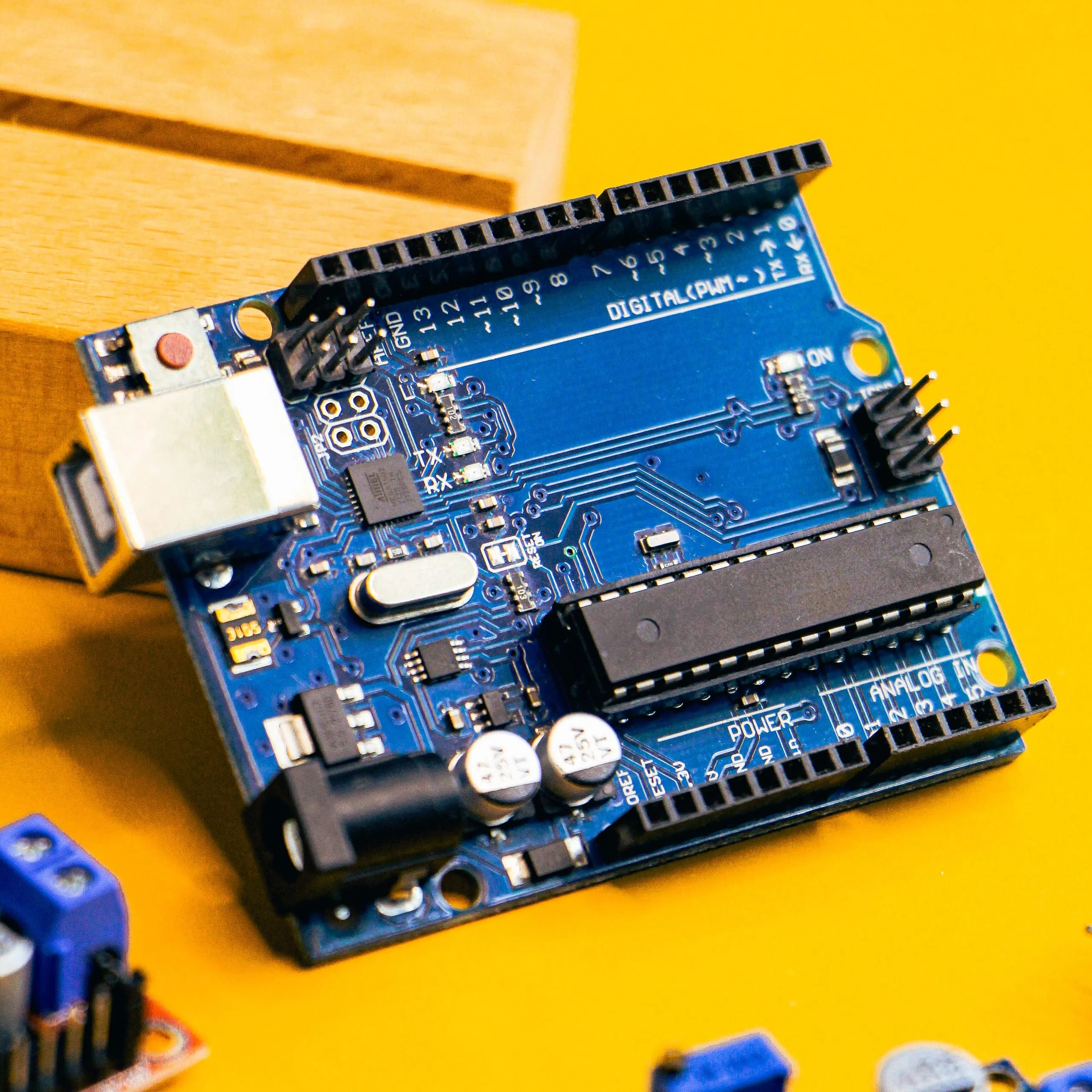 Una scheda Arduino Uno blu appoggiata su un piano giallo, vista dall'alto di tre quarti
