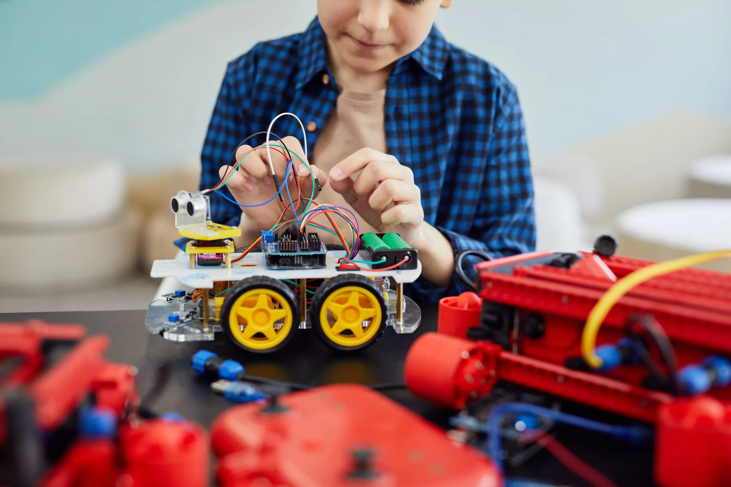 Un ragazzo collega i cavetti di un piccolo robot a quattro ruote con un sensore a ultrasuoni sul davanti